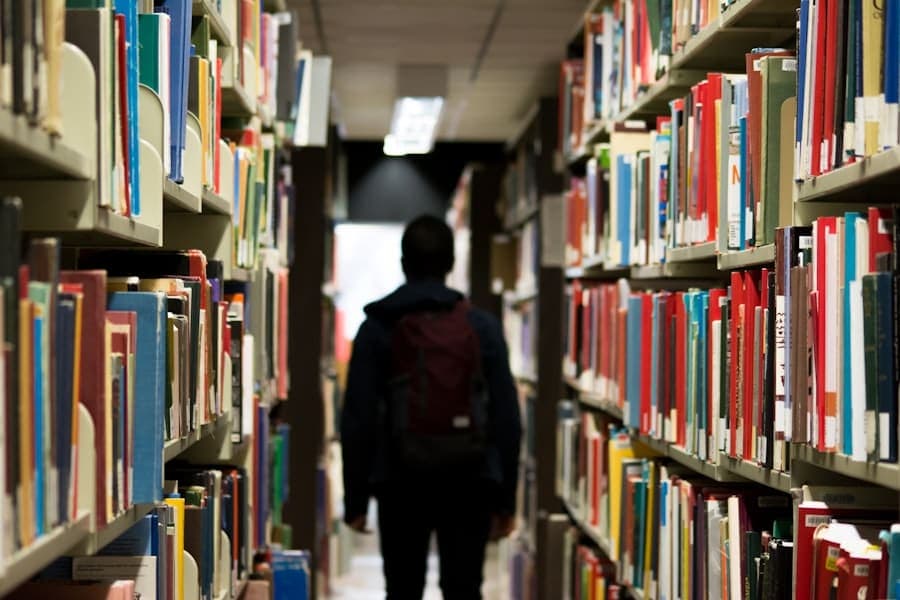 A student with a backpack walking between library shelves